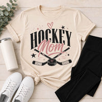 Cream crewneck Hockey Mom graphic tee featuring black and pink lettering with crossed hockey sticks, puck, stars and heart details.