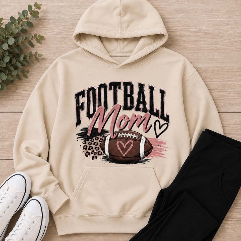 Football Mom shirt featuring a football, heart accents, pink brushstrokes and leopard-print details.