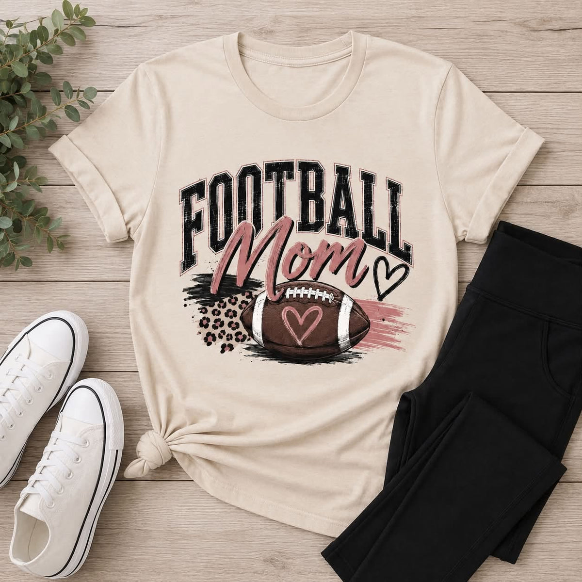 Football Mom shirt featuring a football, heart accents, pink brushstrokes and leopard-print details.