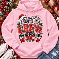 Christmas Crew Making Memories Together graphic on a pink crewneck T-shirt, featuring red lettering, colorful Christmas lights, a Santa hat, holly, and snowflakes.
