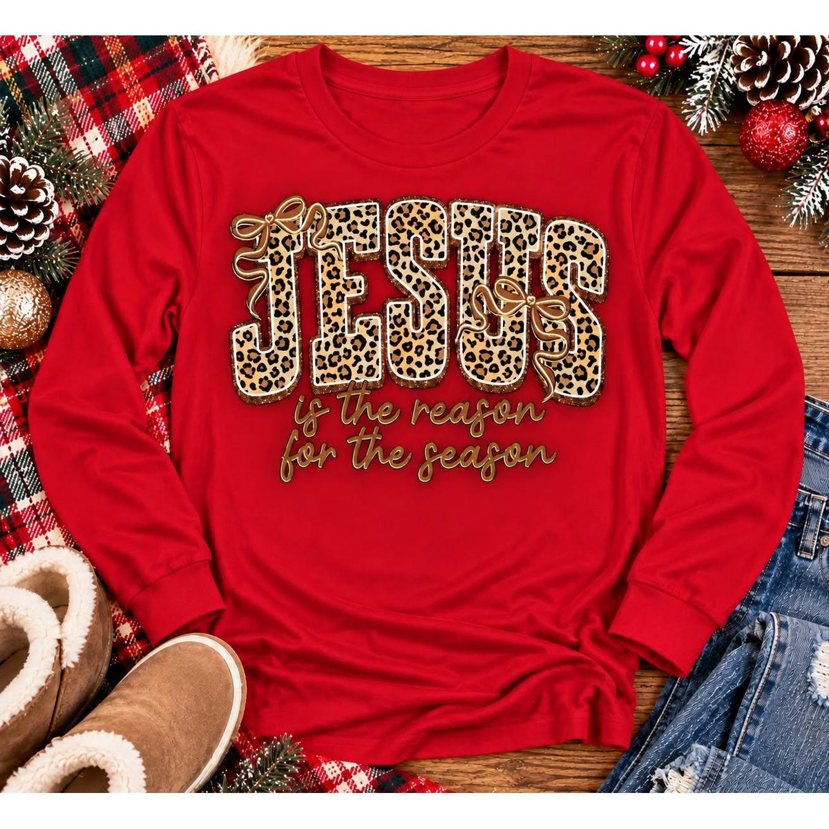Jesus Is the Reason for the Season Christmas graphic shirt featuring bold leopard print JESUS lettering, decorative gold bows, and gold script. Faith-inspired holiday apparel available in red and black with four style options.