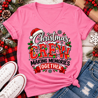 Christmas Crew Making Memories Together graphic on a pink crewneck T-shirt, featuring red lettering, colorful Christmas lights, a Santa hat, holly, and snowflakes.