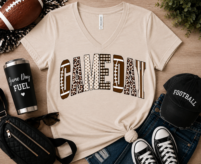 Neutral Game Day graphic t-shirt featuring varsity-style lettering with football, leopard, gingham, polka dot, and striped patterns, styled with jeans and football accessories for fall football season.