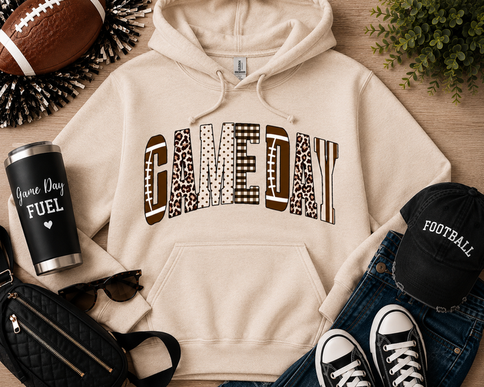Neutral cream Game Day graphic hoodie featuring varsity-style lettering with football, leopard, gingham, polka dot, and striped patterns. Cozy unisex pullover sweatshirt styled with jeans and football accessories, perfect for tailgates, football season, and fall game day outfits.