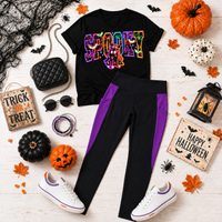 Black V-neck Halloween shirt featuring a colorful SPOOKY ghost graphic, styled with black and purple pocket leggings, white sneakers, and accessories.