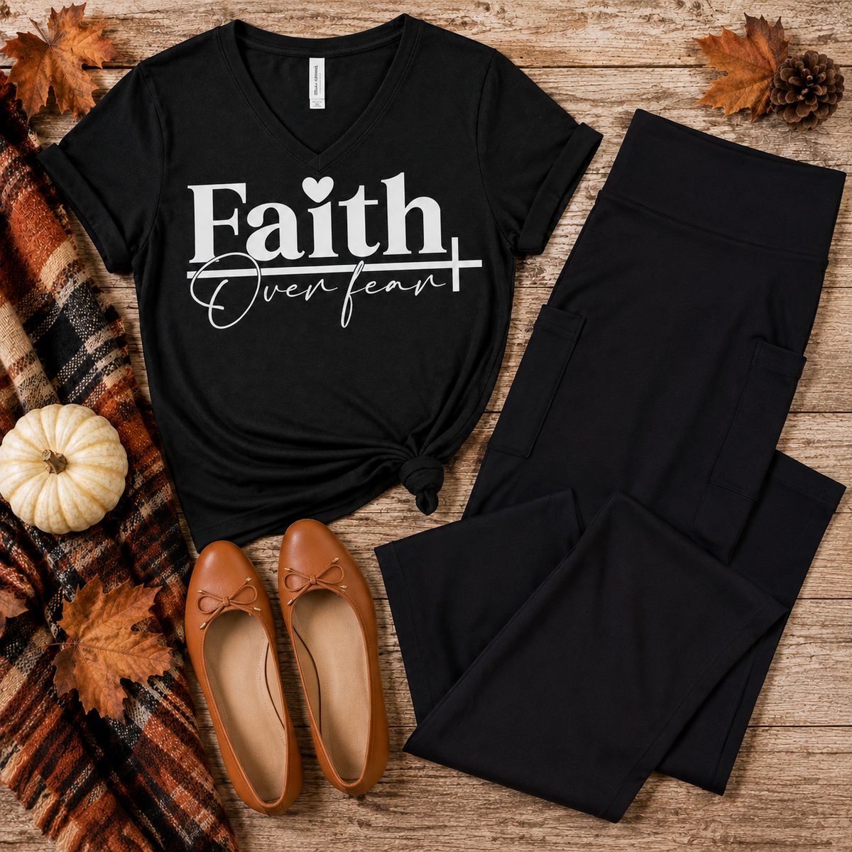 Black Faith Over Fear V-neck graphic T-shirt styled in a fall flat lay with black cropped flare pocket pants, cognac ballet flats, a plaid scarf, autumn leaves, and a white pumpkin.