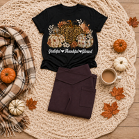 Black crewneck T-shirt featuring leopard and floral pumpkins with white Grateful Thankful Blessed script, styled with folded brown leggings in a fall flat lay.