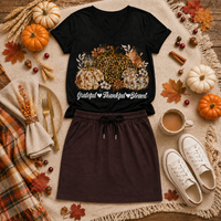 Black V-neck T-shirt featuring leopard and floral pumpkins with white Grateful Thankful Blessed lettering, styled with a brown jogger skirt in a fall flat lay.