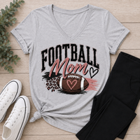 Football Mom shirt featuring a football, heart accents, pink brushstrokes and leopard-print details.