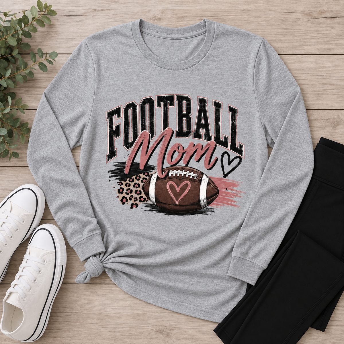 Football Mom shirt featuring a football, heart accents, pink brushstrokes and leopard-print details.