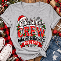 Christmas Crew Making Memories Together graphic on a pink crewneck T-shirt, featuring red lettering, colorful Christmas lights, a Santa hat, holly, and snowflakes.