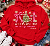 Christian Christmas shirt featuring I Will Praise Him in Every Season Psalm 146:2 graphic with pink bows, decorated Christmas tree, and cream snowflakes.