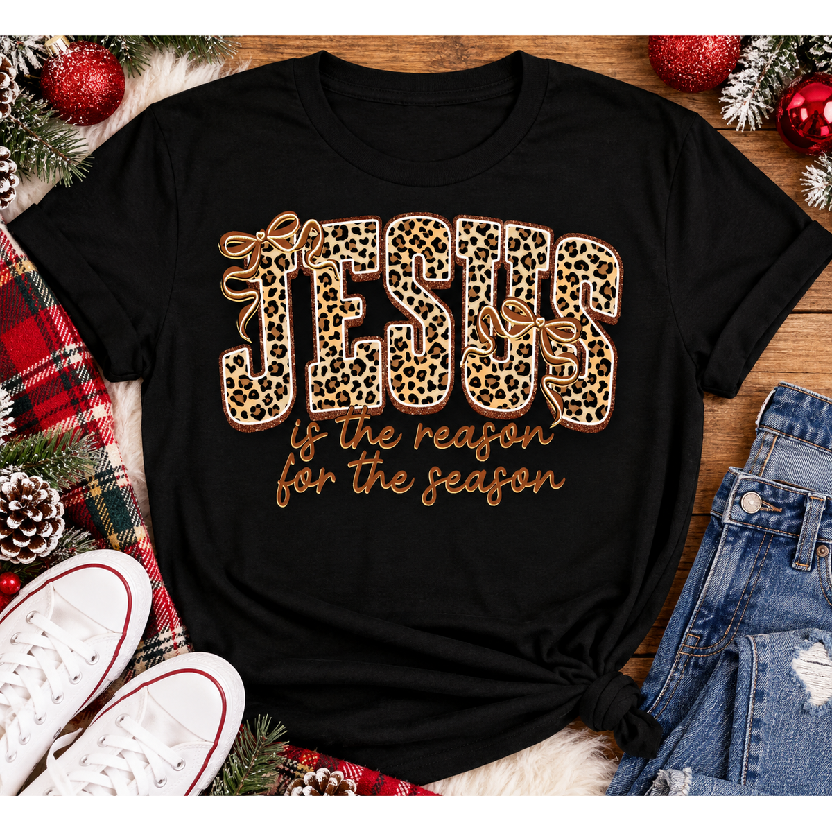 Jesus Is the Reason for the Season Christmas graphic shirt featuring bold leopard print JESUS lettering, decorative gold bows, and gold script. Faith-inspired holiday apparel available in red and black with four style options.