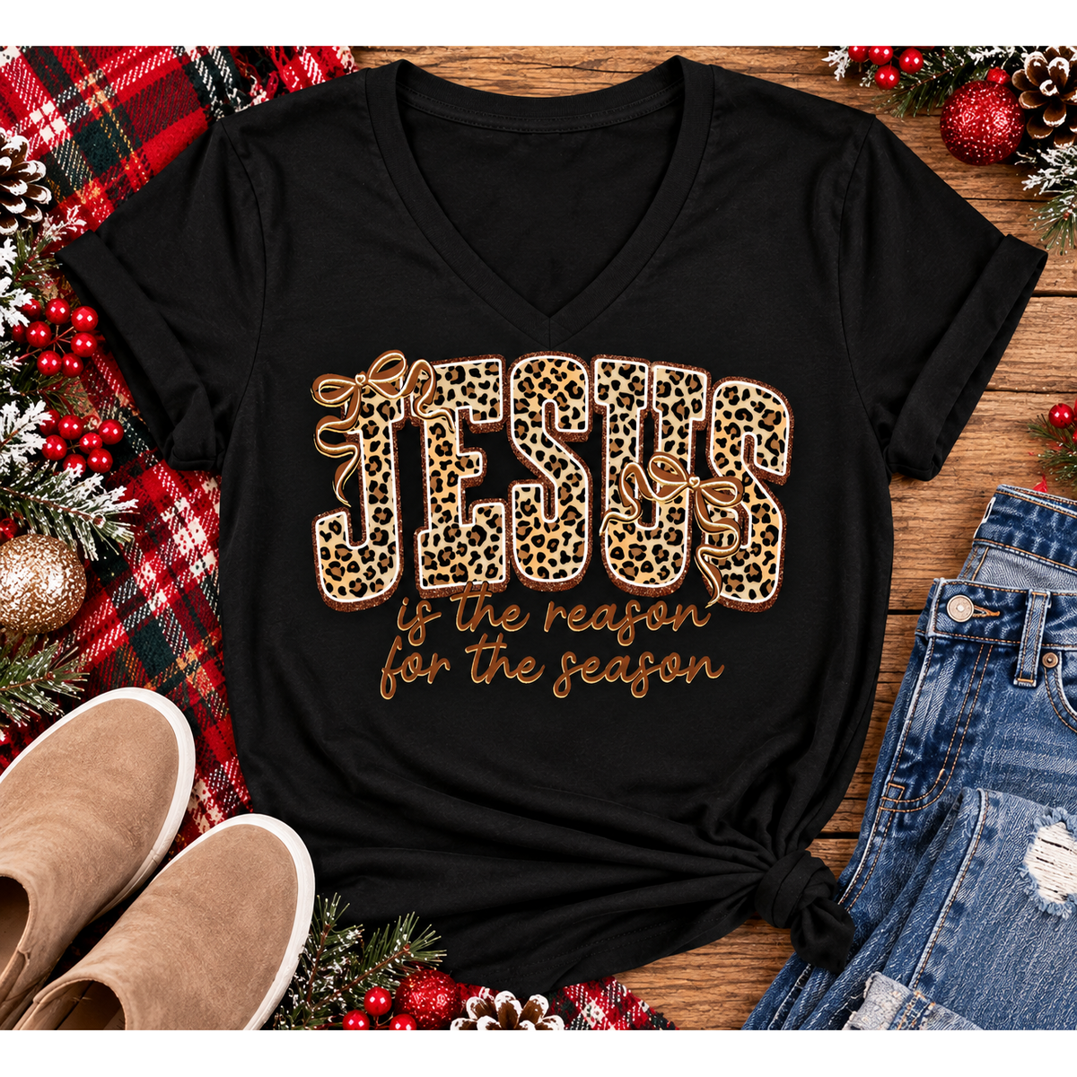 Jesus Is the Reason for the Season Christmas graphic shirt featuring bold leopard print JESUS lettering, decorative gold bows, and gold script. Faith-inspired holiday apparel available in red and black with four style options.