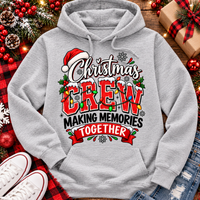 Christmas Crew Making Memories Together graphic on a pink crewneck T-shirt, featuring red lettering, colorful Christmas lights, a Santa hat, holly, and snowflakes.