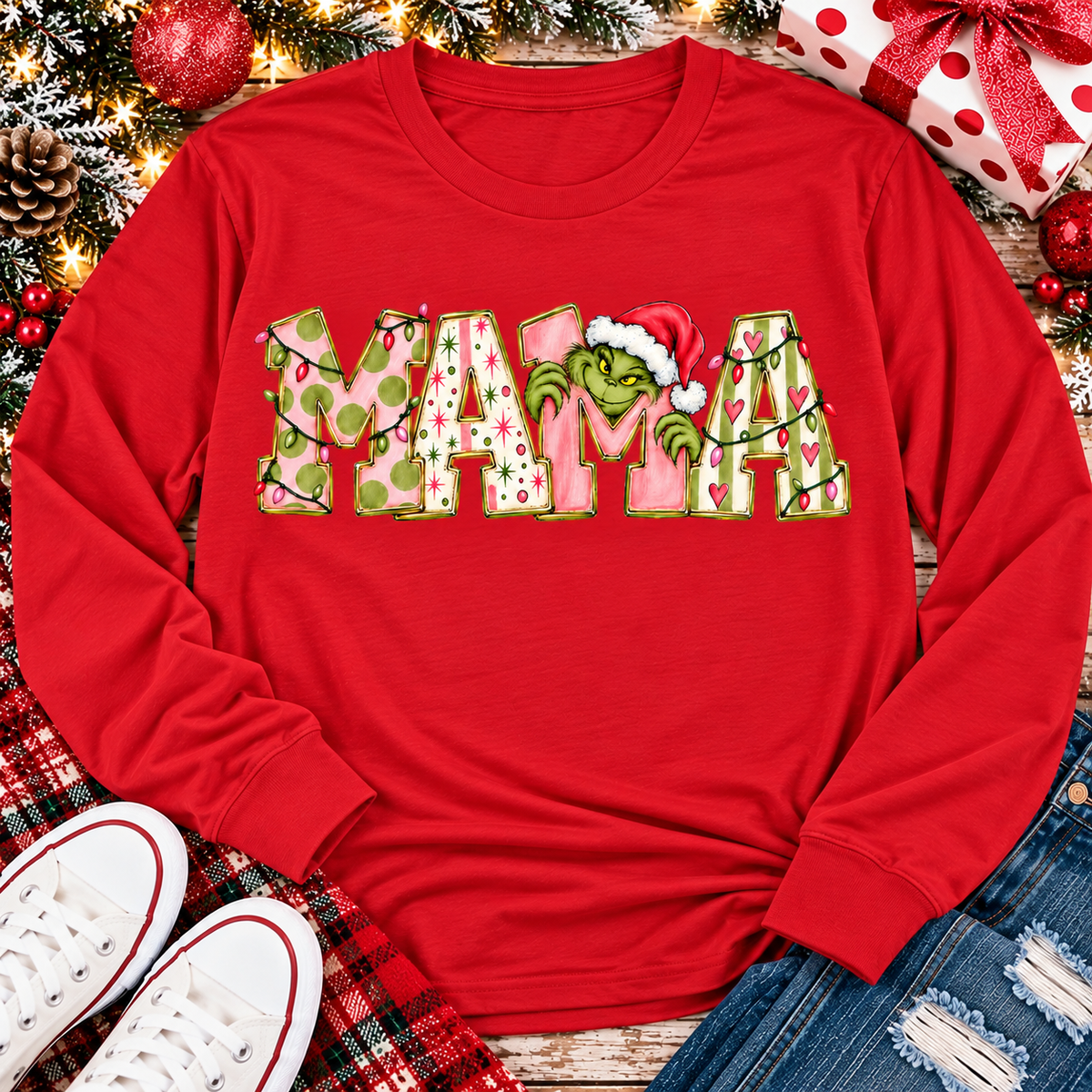 Christmas MAMA graphic shirt featuring pink and green patterned lettering, colorful holiday lights, and a Grinch-inspired character wearing a Santa hat.