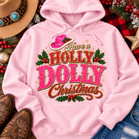 Have a Holly Dolly Christmas western graphic shirt featuring pink and red glitter-inspired lettering, a festive pink cowgirl hat, gold accents, and Christmas holly berries. Available in beige and pink in short sleeve crewneck, V-neck, long sleeve crewneck, and hoodie styles.