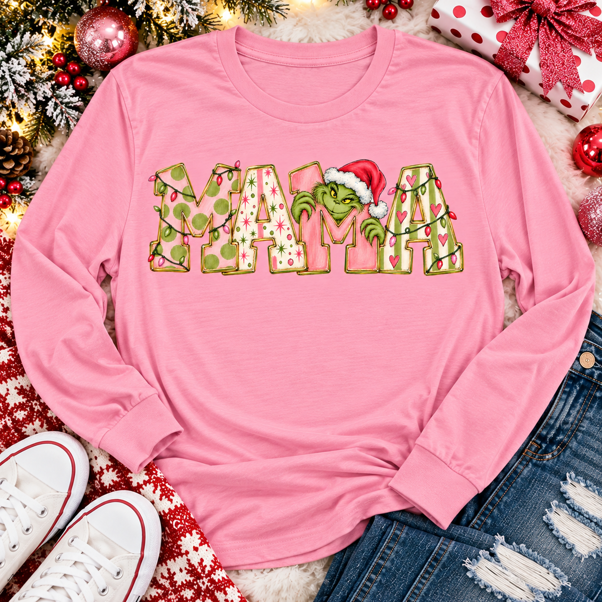 Christmas MAMA graphic shirt featuring pink and green patterned lettering, colorful holiday lights, and a Grinch-inspired character wearing a Santa hat.