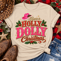 Have a Holly Dolly Christmas western graphic shirt featuring pink and red glitter-inspired lettering, a festive pink cowgirl hat, gold accents, and Christmas holly berries. Available in beige and pink in short sleeve crewneck, V-neck, long sleeve crewneck, and hoodie styles.