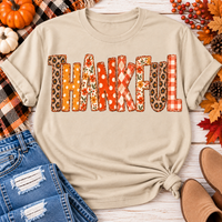 Beige short sleeve crewneck graphic tee with Thankful lettering in orange and neutral fall patterns, styled with distressed jeans.