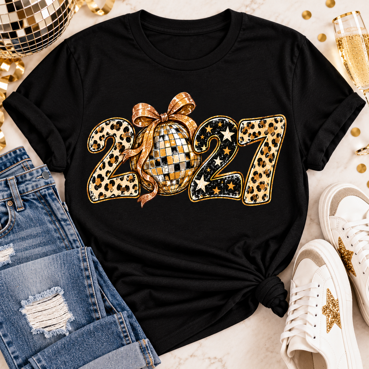 Black 2027 New Year's graphic apparel featuring leopard print numbers, a gold disco ball with an oversized glittery bow, black and gold stars, and sparkling accents. Available in crewneck tee, V-neck tee, sweatshirt, and hoodie styles.