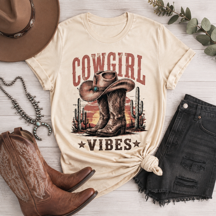 Cowgirl Vibes western graphic apparel featuring cowboy boots, cowgirl hat, cacti and desert sunset design