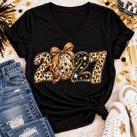 Black 2027 New Year's graphic apparel featuring leopard print numbers, a gold disco ball with an oversized glittery bow, black and gold stars, and sparkling accents. Available in crewneck tee, V-neck tee, sweatshirt, and hoodie styles.