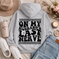 Gray graphic hoodie featuring bold black “On My Husband’s Last Nerve” lettering with checkerboard and sparkle details on the back.