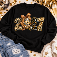 Black 2027 New Year's graphic apparel featuring leopard print numbers, a gold disco ball with an oversized glittery bow, black and gold stars, and sparkling accents. Available in crewneck tee, V-neck tee, sweatshirt, and hoodie styles.